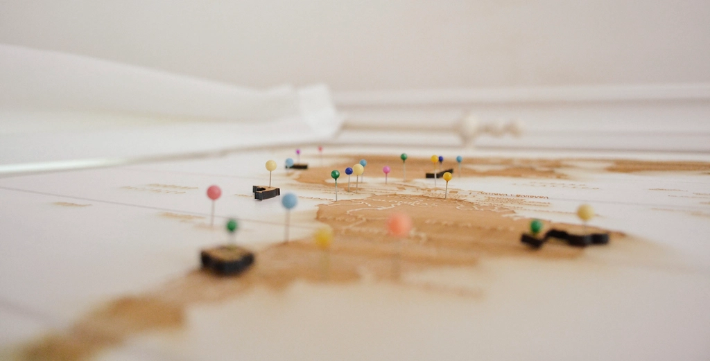 A traveler's hands tracing a route across a paper world map spread on a table beside a passport.
