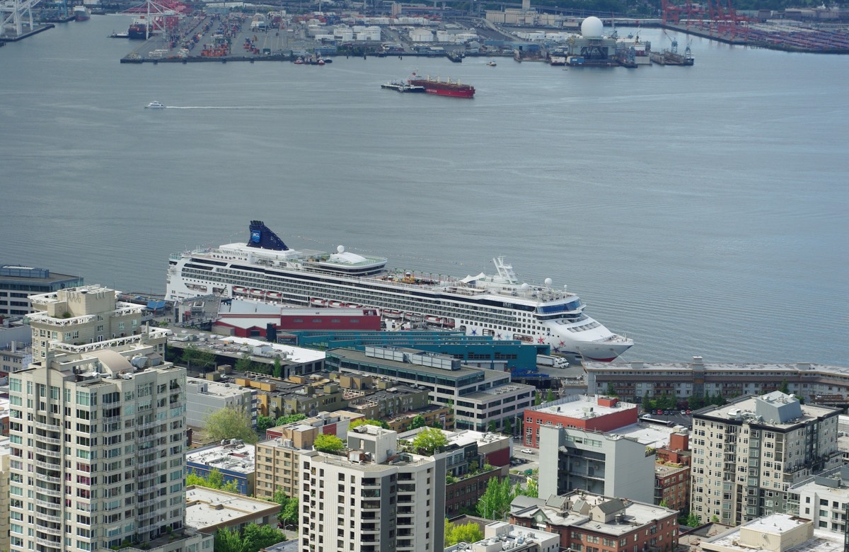 A large cruise ship docked at the Seattle waterfront with the city skyline behind it.