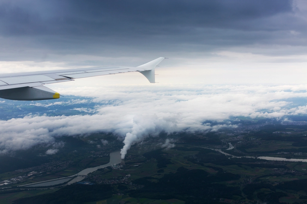 View from a passenger window of an airliner wing cruising above a layer of white clouds.